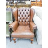 A REPRODUCTION FIRESIDE ARMCHAIR, WITH BROWN HIDE UPHOLSTERY AND BUTTON BACK, A REPRODUCTION