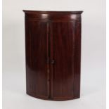 EARLY NINETEENTH CENTURY CROSSBANDED AND LINE INLAID MAHOGANY BOW FRONTED CORNER CUPBOARD, of