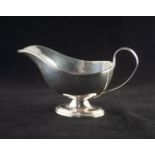 AN EARLY TWENTIETH CENTURY SILVER SAUCE BOAT, with reeded edge, reeded loop handle, standing on an