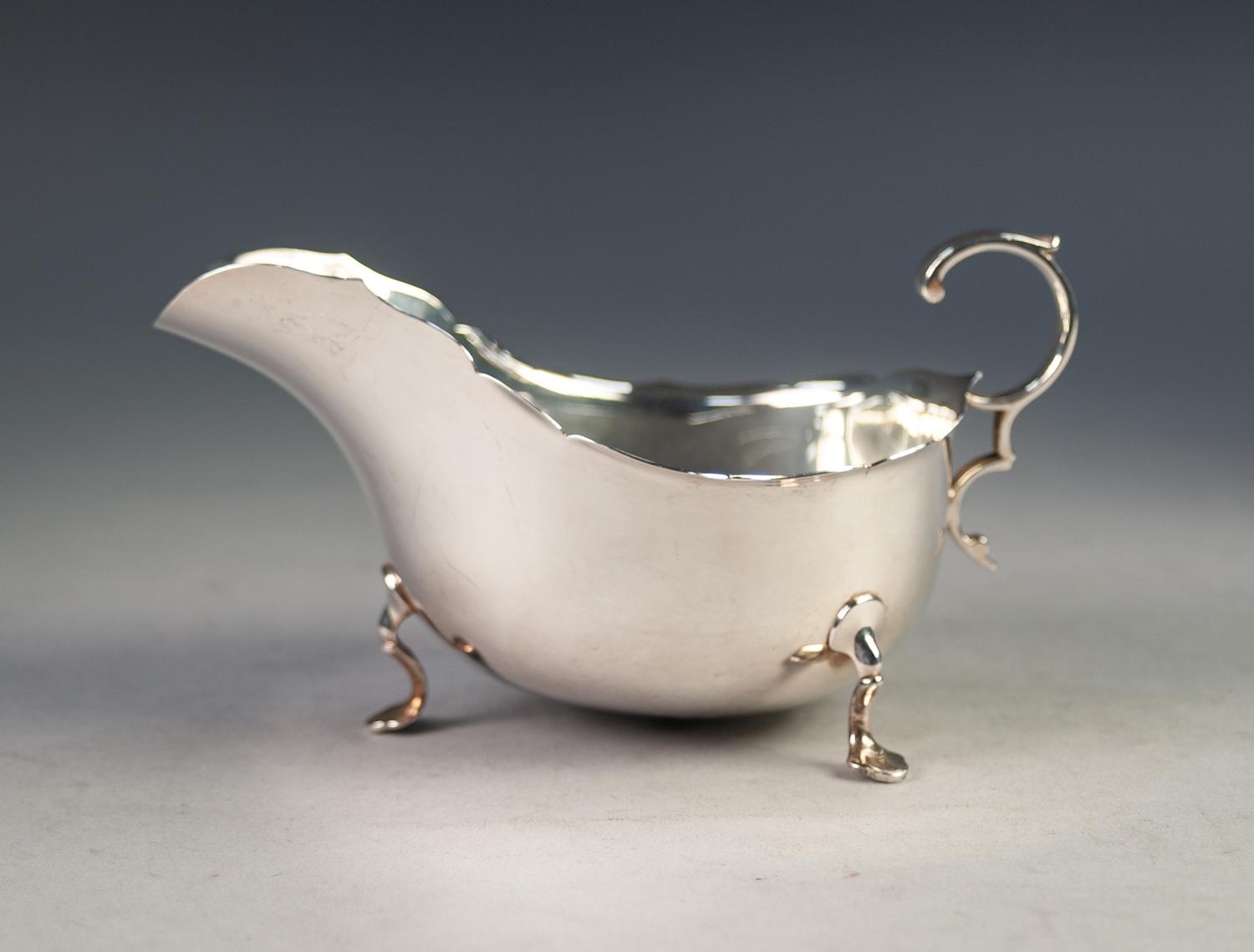 AN EDWARDIAN SILVER SAUCE BOAT, with everted cut rim, flying scroll handle standing on three trefoil