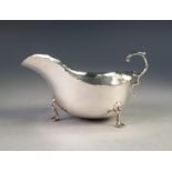 AN EDWARDIAN SILVER SAUCE BOAT, with everted cut rim, flying scroll handle standing on three trefoil