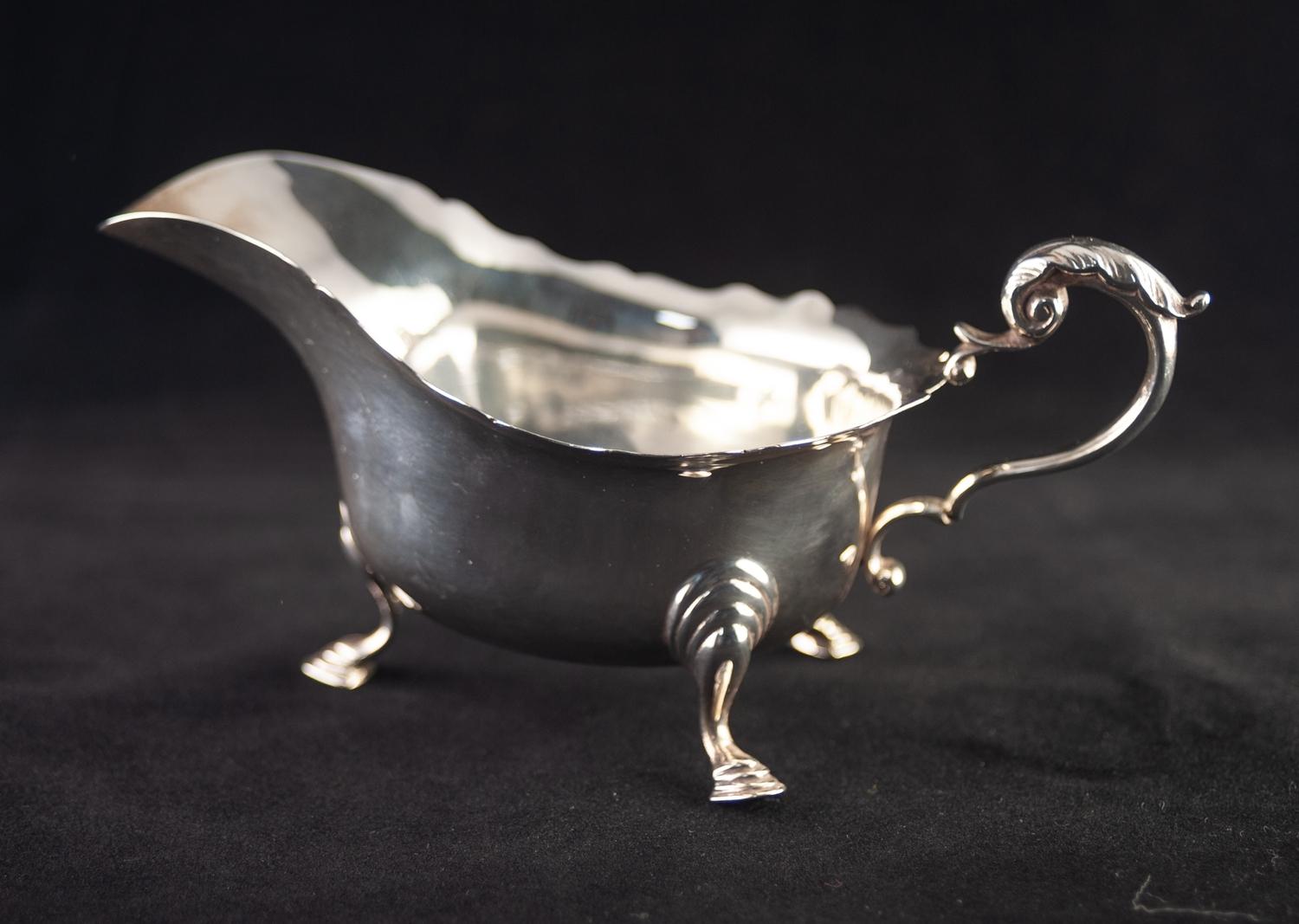 A TWENTIETH CENTURY SILVER SAUCE BOAT with everted cut rim, leaf capped scroll handle, standing on