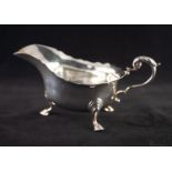 A TWENTIETH CENTURY SILVER SAUCE BOAT with everted cut rim, leaf capped scroll handle, standing on