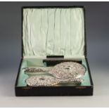 GEORGE V CASED THREE PIECE EMBOSSED SILVER BACKED DRESSING TABLE HAND MIRROR AND BRUSH SET, repousse