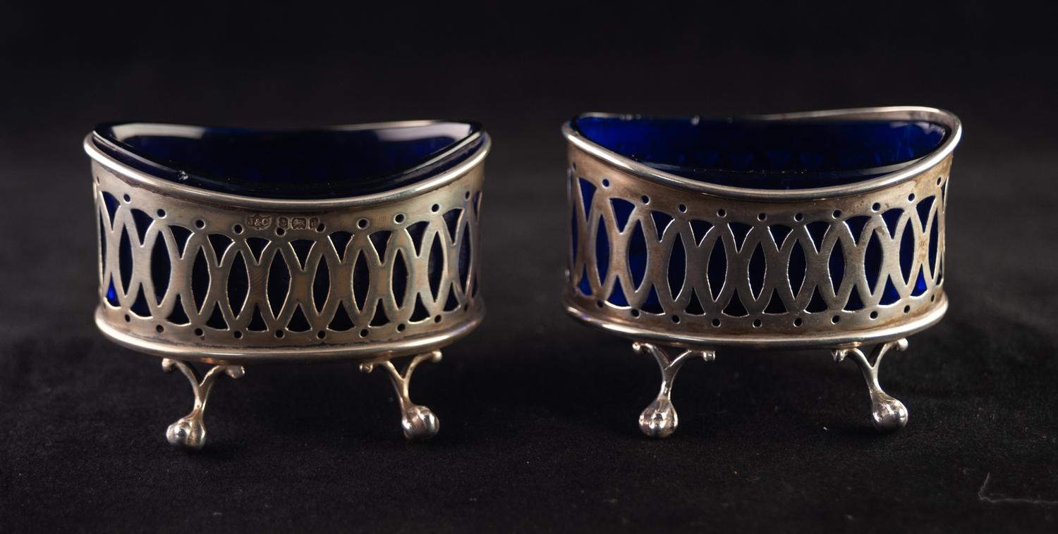 A PAIR OF EDWARDIAN OVAL SILVER SALT CELLARS, with blue glass liners, each standing on four claw and