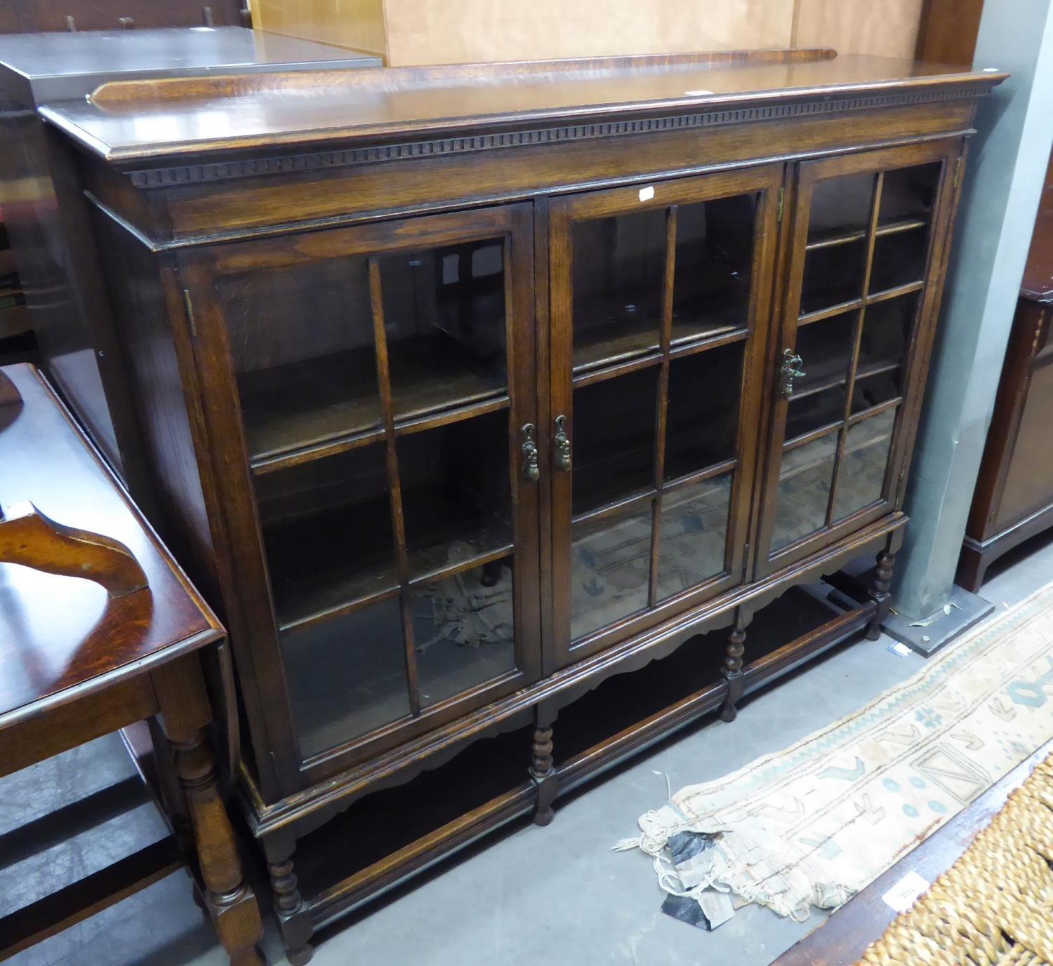 AN OAK LIBRARY BOOKCASE, ENCLOSED BY THREE PANE PANEL DOORS, ON BOBBIN TURNED SUPPORTS WITH PLAIN