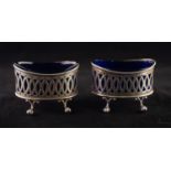 A PAIR OF EDWARDIAN OVAL SILVER SALT CELLARS, with blue glass liners, each standing on four claw and