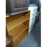 A TEAK THREE TIER OPEN BOOKCASE; A BLACK ASH THREE TIER OPEN BOOKCASE; A WHITE PAINTED WOOD