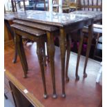 A MID TWENTIETH CENTURY MAHOGANY NEST OF THREE TABLES, HAVING GLASS PROTECTOR TOPS, ALL RAISED ON