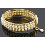 An Eastern yellow metal hinged and river pearl set bangle