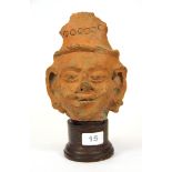 An early Indian terracotta deity head on a wooden base, H. 25cm (including base).