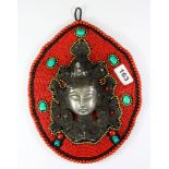 A Tibetan silvered metal head of a female deity set onto a beaded wall hanging, H. 27cm.