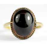 A yellow gold (stamped 18ct shank and 9ct setting) cabochon cut garnet set ring, (W).