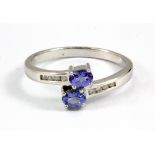 A 9ct white gold crossover ring set with oval cut tanzanites and diamonds, (M.5).