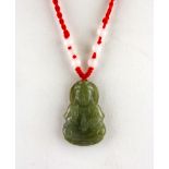 A carved olive green jade amulet of the goddess Guanyin on a red silk adjustable neck cord,
