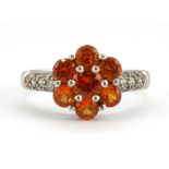 A 925 silver orange topaz cluster ring with white stone set shoulders, (T).