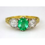 A yellow metal (tested 18ct gold) ring set with an oval cut emerald flanked by old cut diamonds,