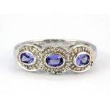 A 9ct white gold ring set with three oval cut tanzanites and diamonds, (L.5).