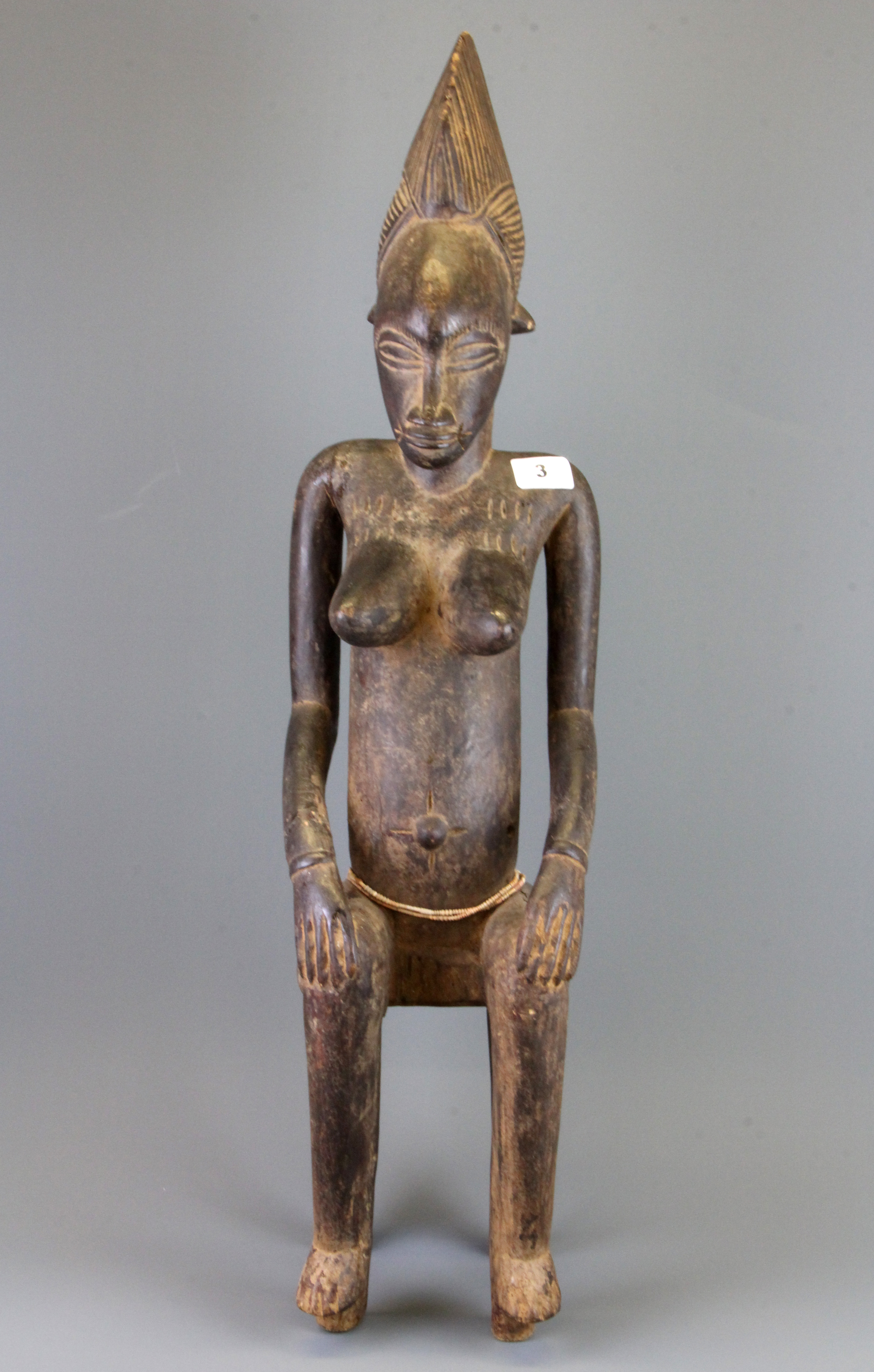 A tall African Punu tribal carved wooden figure of a woman sitting on a stool, H. 78cm.