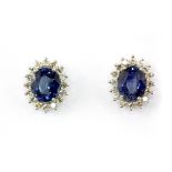 A pair of 18ct white gold (stamped 750) cluster earrings set with an oval cut sapphire surrounded by