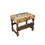 A Charles II walnut stool, upholstered with a needlepoint seat, with carved stretcher rail, on