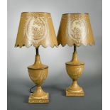 A pair of toleware table lamps and shades, the urn form bases decorated with foliate scrolls, the