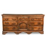 A George III oak dresser base, of two small drawers and a central arched cupboard, flanked by six