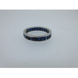 A sapphire full hoop eternity ring, channel set with calibré cut sapphires, unmarked white metal