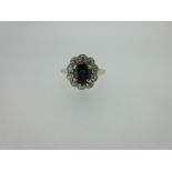 A sapphire and diamond cluster ring, the oval cut sapphire four claw set above a petal edge border