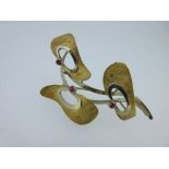 A modern Italian abstract spray brooch set with rubies, designed as twin arched ribbon stems with