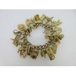 A 9ct gold charm bracelet with a large quantity of charms, the curb link bracelet with padlock catch