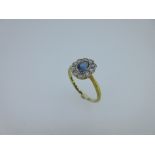 A sapphire and diamond oval cluster ring, the oval cut light-mid blue sapphire in a millegrain