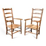 A pair of Arts and Crafts ash ladder back armchairs, each with shaped arms over rush seats (2) 105cm