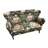 In the manner of Finn Juhl, a small wing back two-seat sofa, in floral upholstery raised on swept