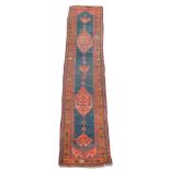 A North Persian corridor runner, with a figured rust red ground pole medallion on a dark blue field,