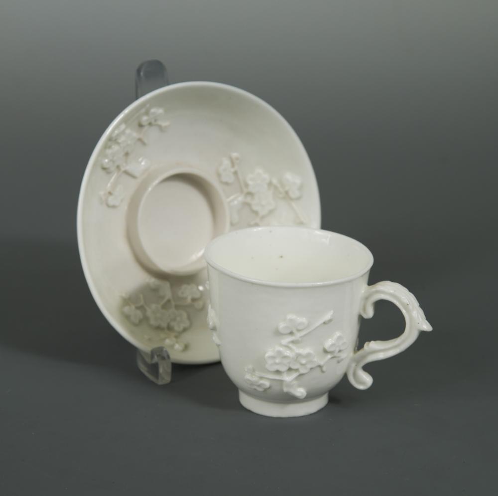 A Saint-Cloud blanc de chine trembleuse cup and saucer, circa 1720-40, with moulded and applied