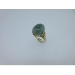 A jadeite jade ring with cast floral shoulders, the oval cabochon jade of mottled sage green,