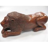 A carved and stained pine model of a recumbent lion, 59 cm wide