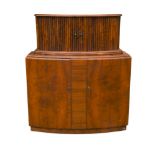 An Art Deco bow front walnut cocktail cabinet, the tambour sliding doors opening to reveal a
