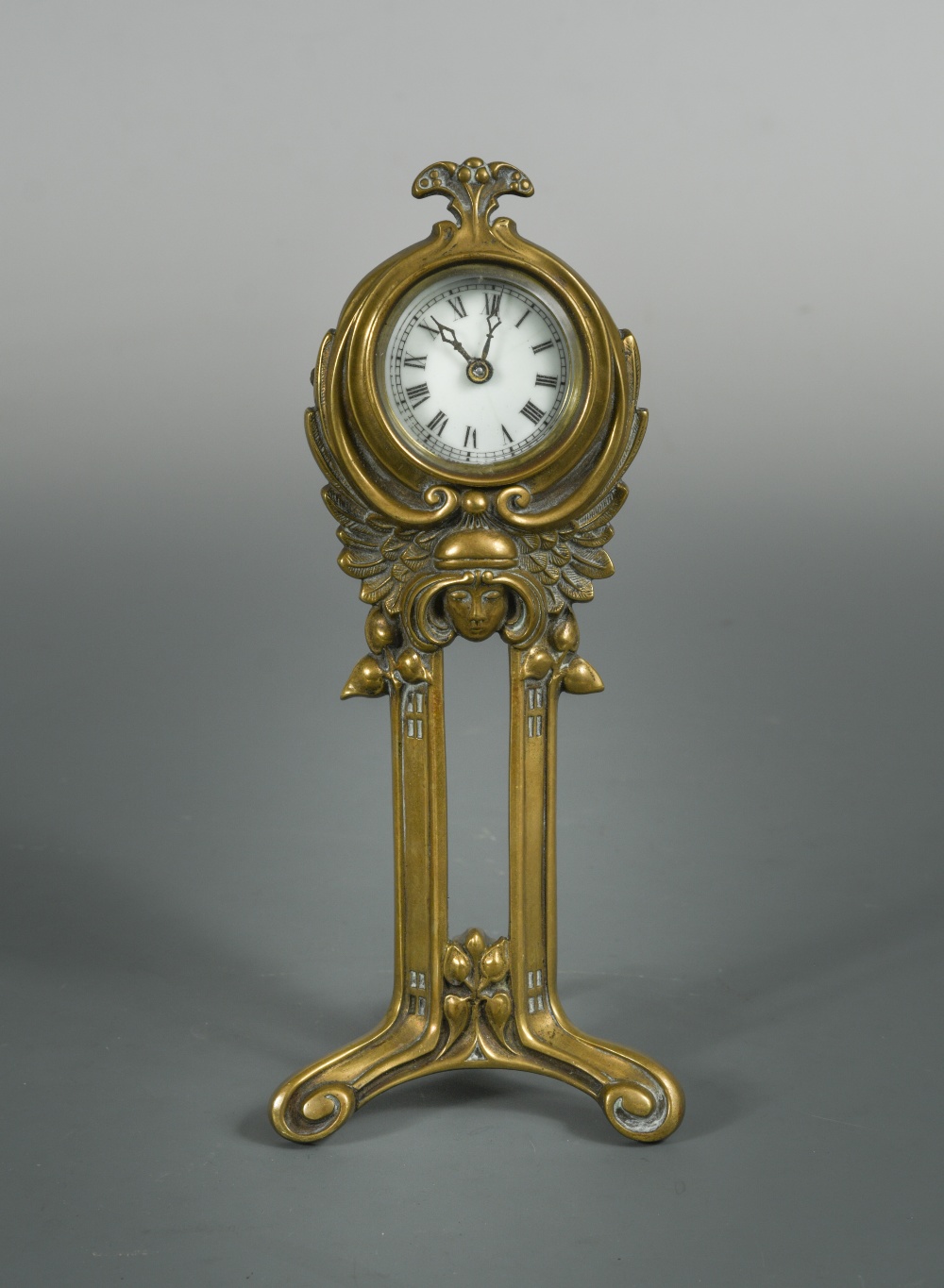 An Art Nouveau brass desk clock by the British United Clock Co., the enamelled dial above a female