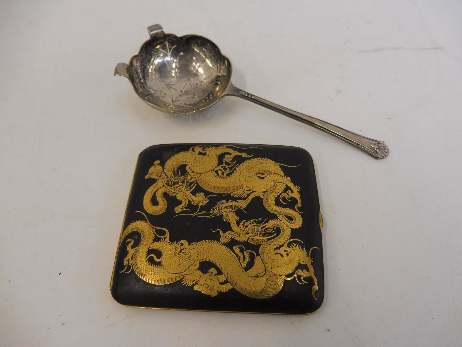 A silver strainer/sifting spoon and an Oriental lacquered cigarette case.