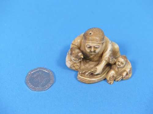 A 19th century Japanese carved ivory Netsuke, depicting a man and boy with a small bird, signed on