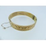 A 9ct yellow gold hinged Bangle, the front and reverse with textured surface and incised decoration,