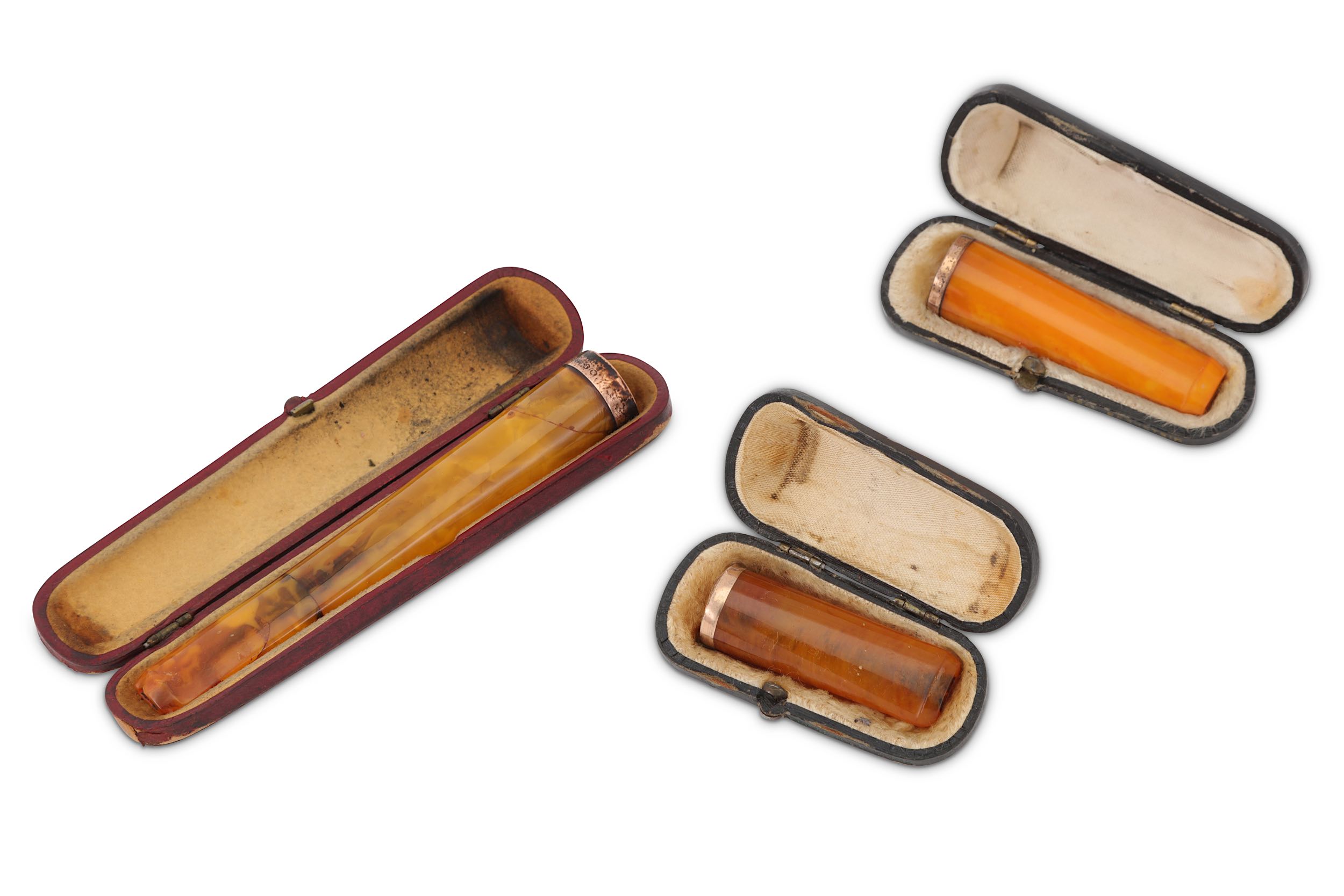 Three cased amber coloured cheroot holders, one with a 9ct gold mount