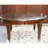 An Edwardian oak dining table, the oval top with extending mechanism, two extra leaves,