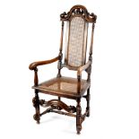 A walnut armchair of Carolean design with cane seat and arch back on scroll front legs