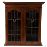 An Art Nouveau oak wall hanging display cabinet, enclosed by stylised leaded glass doors,