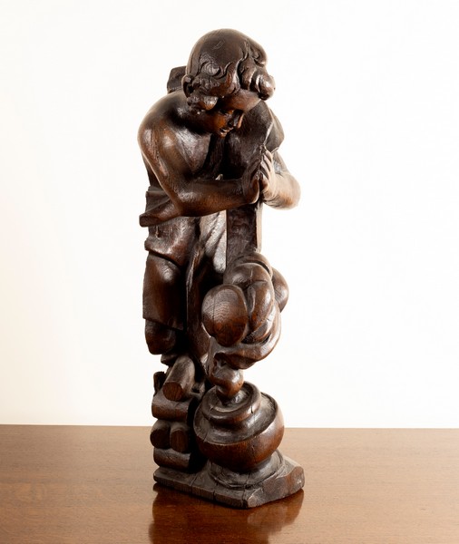 A carved oak wooden figure of a boy by a cooking pot,