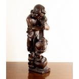 A carved oak wooden figure of a boy by a cooking pot,