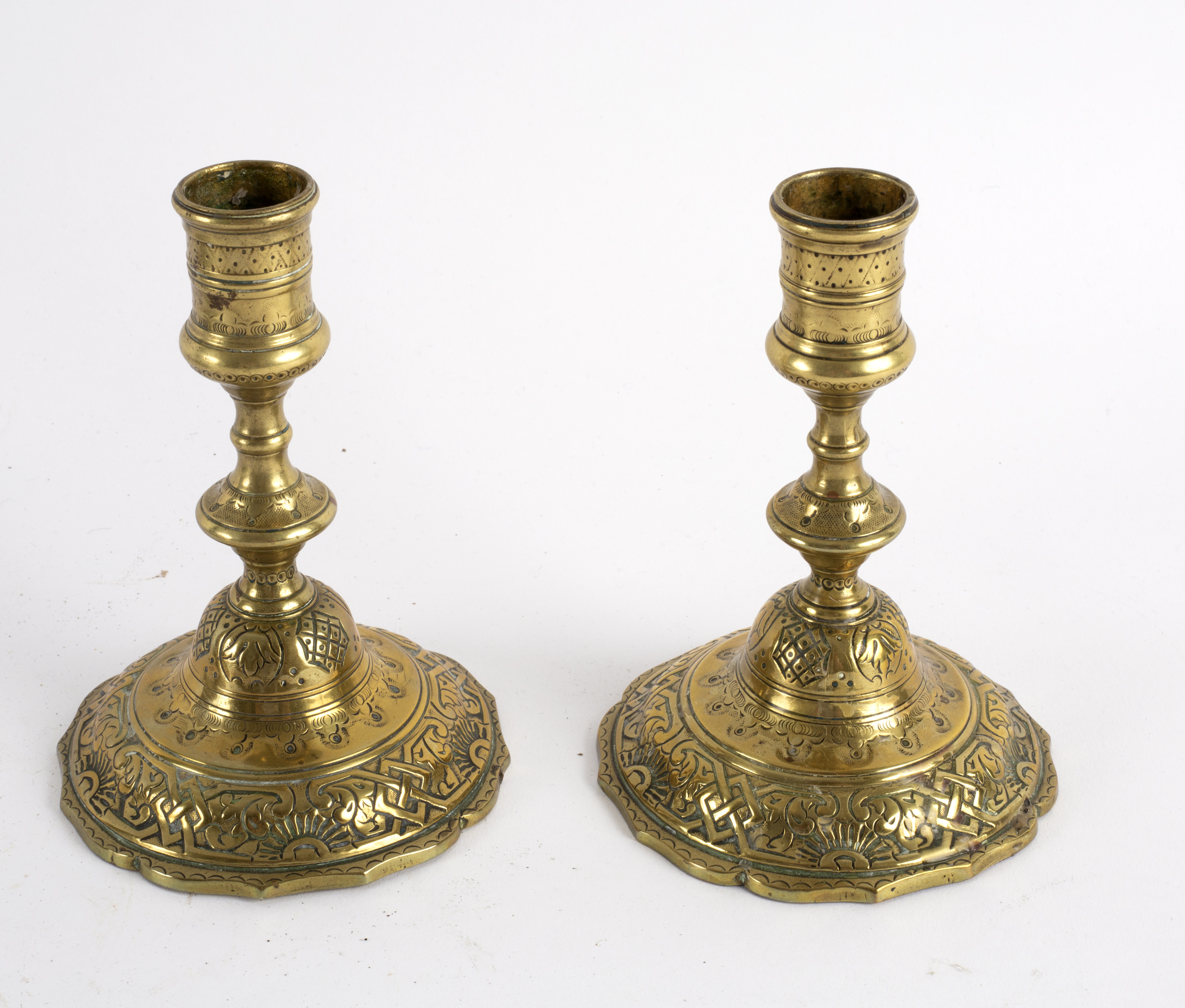 A pair of engraved brass candlesticks on skirt bases, 14.